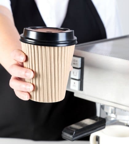 Photo of a Barista handing you a coffee in a disposable paper takeaway cup.