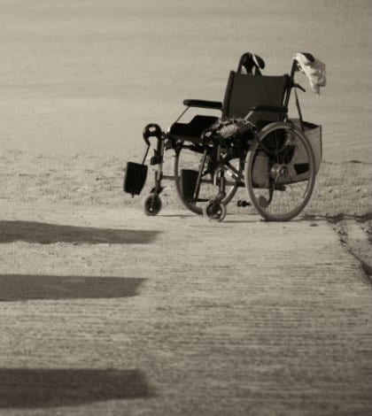 Monochrome image of an abandoned empty wheelchair parked on the edge of sand as it was not able to be wheeled any further over the soft terrain