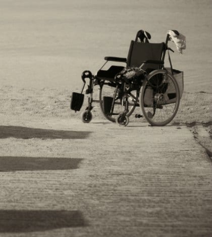 iStock_000020915186 WHEELCHAIR ON SAND 420 Monochrome image of an abandoned empty wheelchair parked on the edge of sand as it was not able to be wheeled any further over the soft terrain