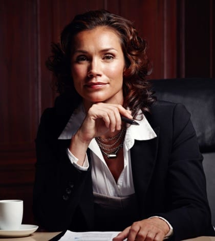 Attractive mature legal woman sitting and leaning on her hand while smiling slightly at the camera