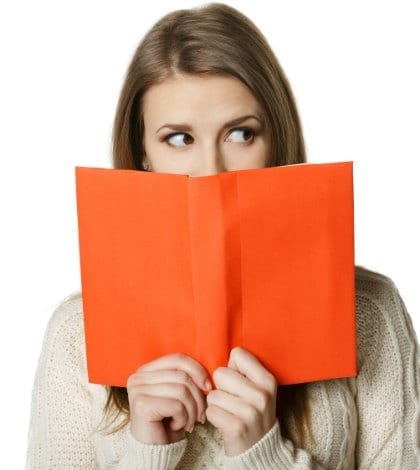 iStock_000023970920 BEHIND BOOK 420 Closeup of young woman peeking over the edge of the opened book, looking to the side at blank copy space, over white background