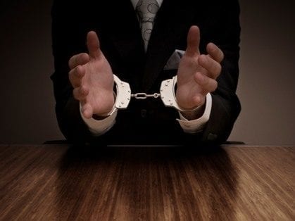 Businessman in handcuffs sitting at table, selective focus on hands