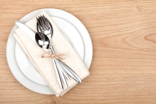 Empty plate and silverware set on wooden table