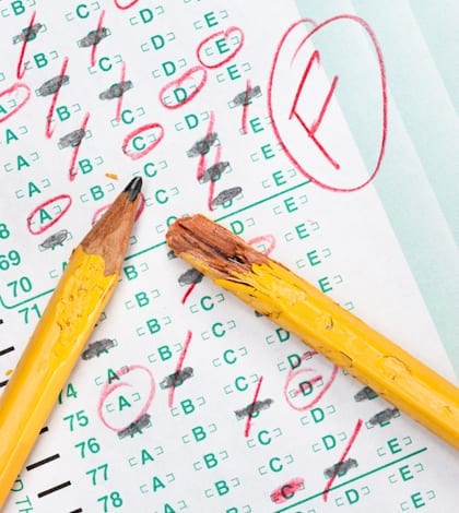 A graded test form with red scoring pencil marks indicates frustration and failure in the education system.