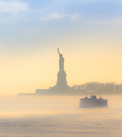 Staten Island Ferry cruises past the Statue of Liberty on a misty sunset. Manhattan, New York City, United States of America. Square composition.