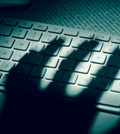 A menacing hand's shadow on a computer keyboard in front of printed computer data. Dramatic light, high contrast.