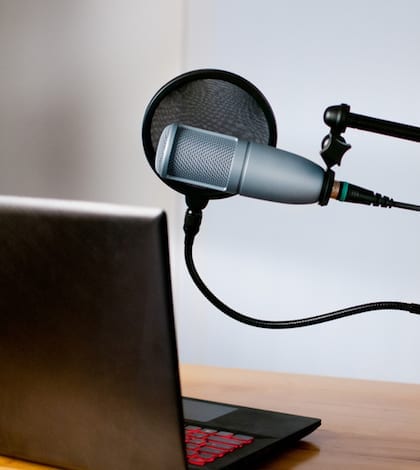 Studio microphone and a laptop sit on a desk Horizontal image of audio equipment and a laptop sitting on a desk in a small sound room. The studio microphone is on a boom and has a pop filter in place. The laptop is open and ready to use.
