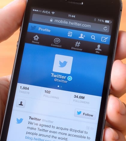 Twitter ?stanbul, Turkey - January 20, 2015: Hand holding a iPhone 5s displaying Twitter, on a wooden background. iPhone is a touchscreen smart phone produced by Apple Inc.