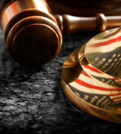 A gavel and the American flag reflected in the base of a justice scale