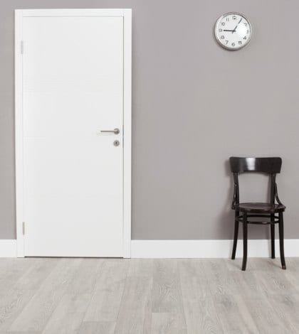 Two wooden chairs in a waiting room with a clock hanging on the wall above them