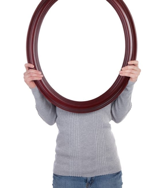 A woman holding a blank oval frame over her face.