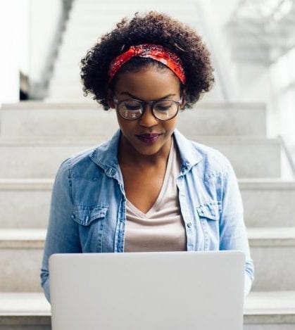 Focused young African student sitting on stairs using a laptop Focused young African female college student working on a laptop on some stairs on campus preparing for an exam