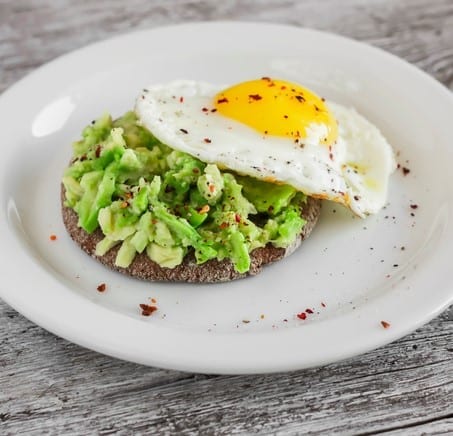 sandwich with avocado and a fried egg on a white plate on a light rustic wood surface