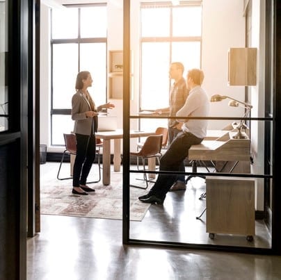 Businesswoman explaining strategy to colleagues seen through glass walls in office. Female professional is giving presentation to executives in board room. All are in meeting.