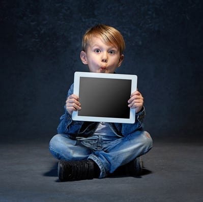 Little boy sitting with tablet in gray studio