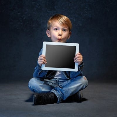 Little boy sitting with tablet in studio Little boy sitting with tablet in gray studio