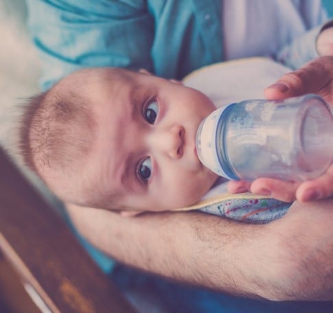 Close up of a baby boy drinking milk from a bottle given by his father