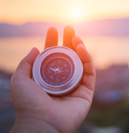 Closeup hand holding compass with mountain and sunset sky background. Closeup hand holding compass with mountain and sunset sky background.