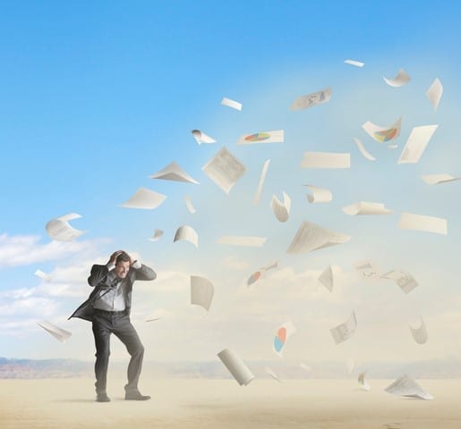 Headwinds A businessman fighting through a sandstorm with a lot of paperwork being tossed in the air.
