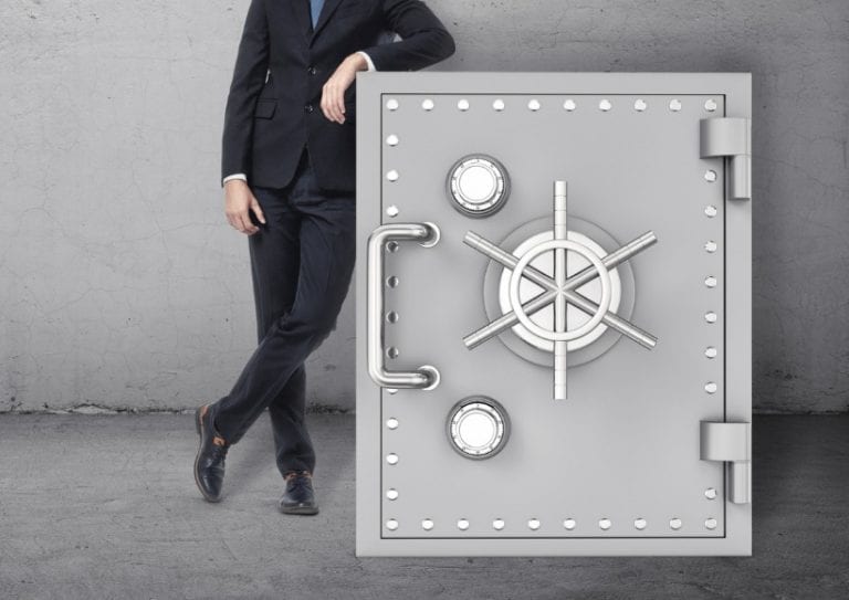 businessman-in-confident-pose-standing-next-to-the-safe-picture-id624991814 A businessman in a confident pose standing next to the safe on the background of the grey wall. Business and finance. Success and wealth. Protection of funds.