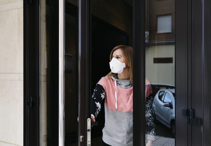 Woman goes out to the street from the door of her house with a face mask A woman goes out to the street from the door of her house with a face mask