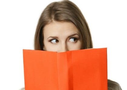 000023970920 Peek BEHIND BOOK suspicious wary 420 Closeup of young woman peeking over the edge of the opened book, looking to the side at blank copy space, over white background