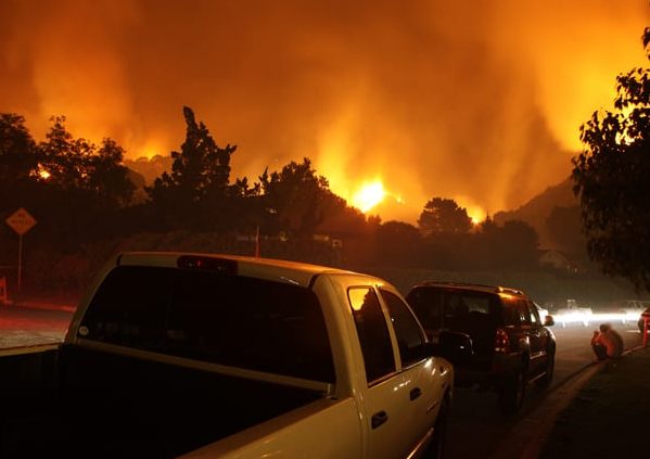 Neighborhood On Fire At Night Residents of a neighborhood sit by and watch a fire threaten their homes.