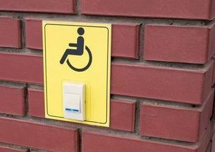 Assistance button for disabled people at the entrance of the iron gate. A disabled sign on a wall, concept image.