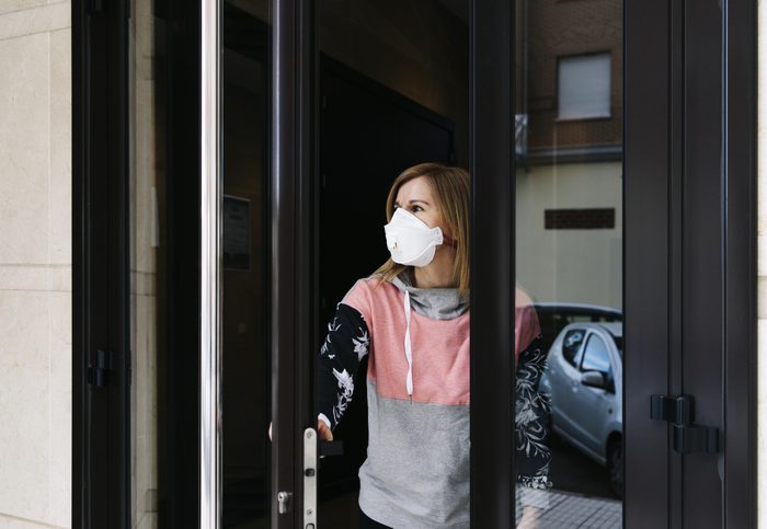 Woman goes out to the street from the door of her house with a face mask A woman goes out to the street from the door of her house with a face mask