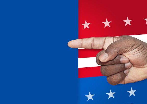 An African man's hand pointing at a blank sign on a US flag themed background. Black man's hand pointing with blank sign on US stars and stripes election background