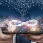 hands holding device with infinity symbol, skyline and constellations in background
