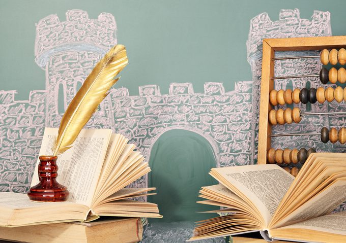 Unusual world of grade school Quill pen, book open, castle and abacus in the background.