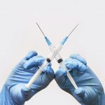 Gloved hands holding vaccine needles crossed.