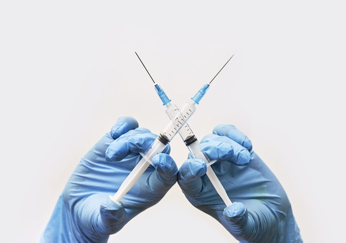 Anti vaccine or anti vaxxer compaign concept Gloved hands holding vaccine needles crossed.