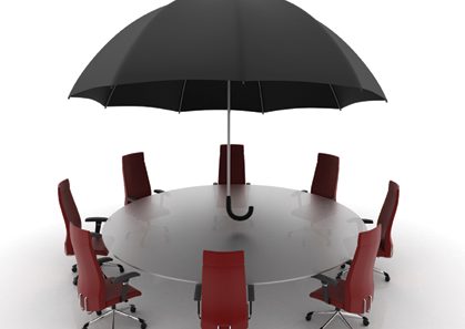 Umbrella over empty chairs around a conference table.