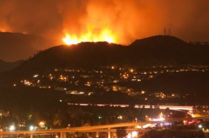 Wildfire in distant hills at night, city and city lights in foreground.