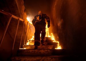 Firefighter walking up stairs in a burning building.