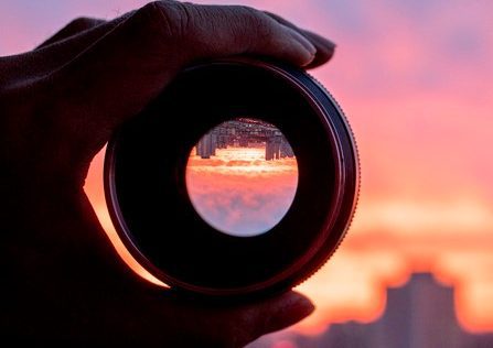 hand holding camera lens, looking at scenics of glowing clouds at sunset Blurred sklyline in the distance being viewed through a hand-held lens up close.