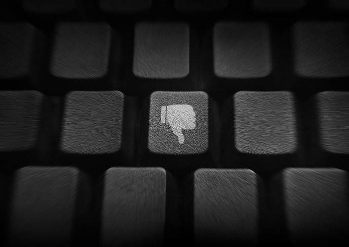 thumb down or dislike button on keyboard. Shadowy image of part of a keyboard, with one key more well lit. On it is an image of "thumbs down."