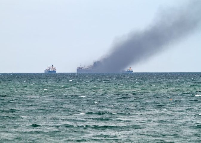 Distanct view of ocean vessel with smoke rising from a fire on board.