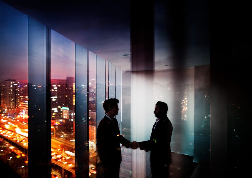 businessmen-shaking-hands-in-office-at-night-with-city-view-picture-id637945960