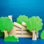 Illustration of toy wood house with green-leaved wood block trees around it.