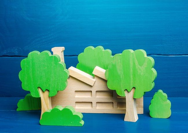 Industrial factory plant hidden behind the trees. Greenwashing concept. PR and trend about caring for environment. Misleading customers and buyers of products and maximizing profits. Hiding facts Illustration of toy wood house with green-leaved wood block trees around it.