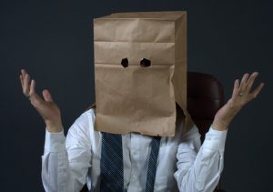 Man wearing suit with bag over his head, shrugging as if he is clueless.