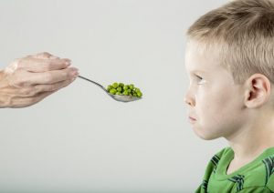 A kid with a sour look on his face, rejecting a spoonful of peas.
