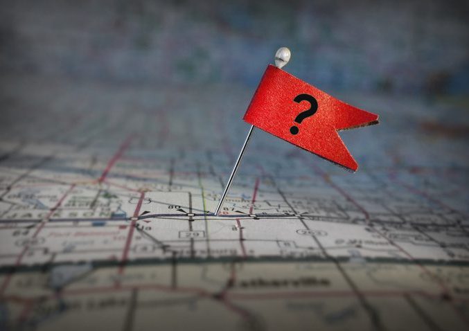 question mark flag on a map Unidentifiable section of a roadmap on which there is a pin. On the pin is a red flag with a question mark on it.