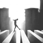 Surreal image in slhouette; man walking across beam-like structure with cityscape in background.