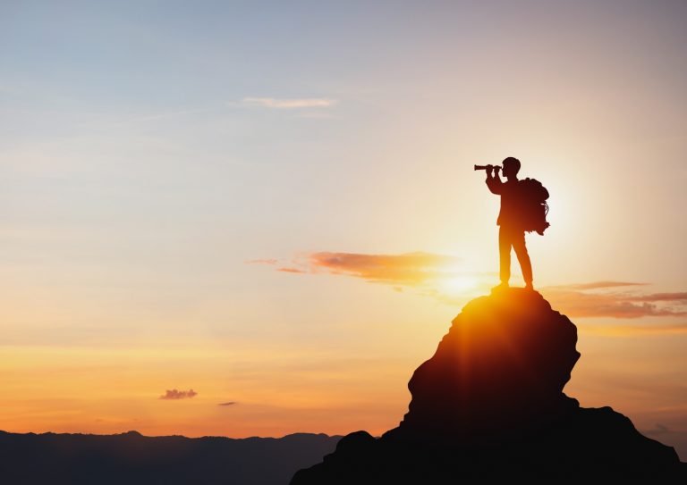 silhouette-of-man-holding-binoculars-on-mountain-peak-against-bright-picture-id1383796215
