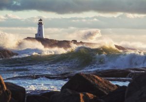 Waves battering a seacoast, with a lighthouse in the background.