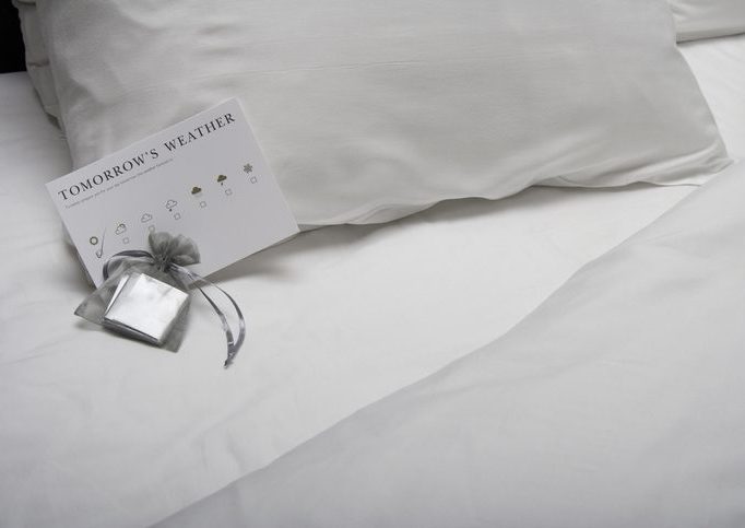 Close-up of chocolates on a turned-down hotel bed Close-up of a pillow with a chocolate and weather report card next to it, as if in a hotel room.